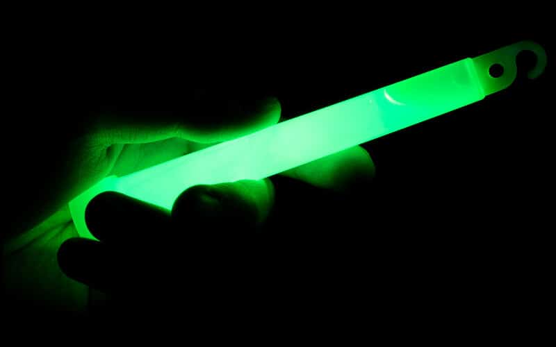 A person's hand holding a green glow stick in the dark.