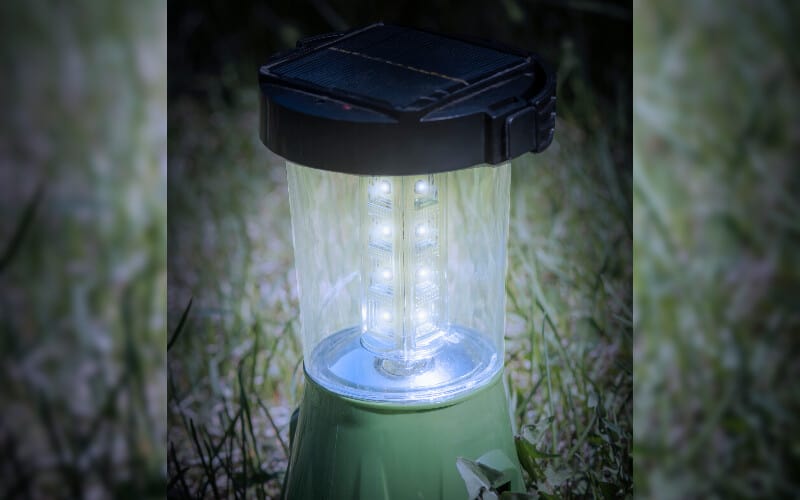 A close up of a solar-powered camping lantern on the grass at dusk.