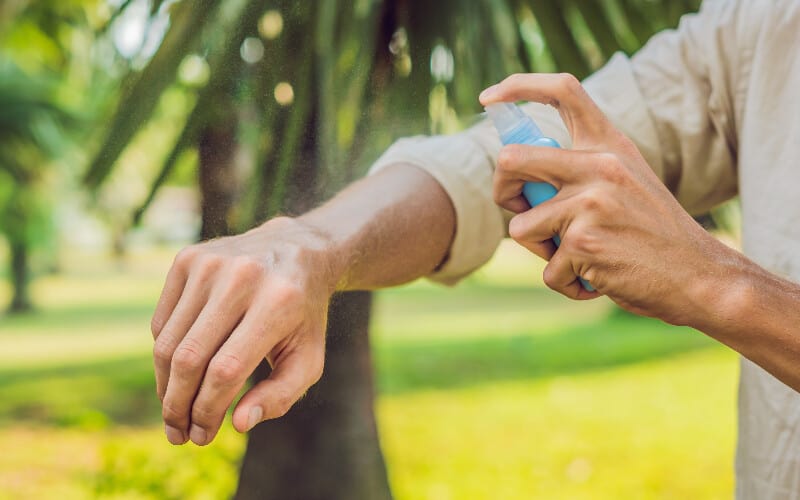 Close-up of a man spraying his arm with DEET based spray - one of the best camping mosquito repellent options.