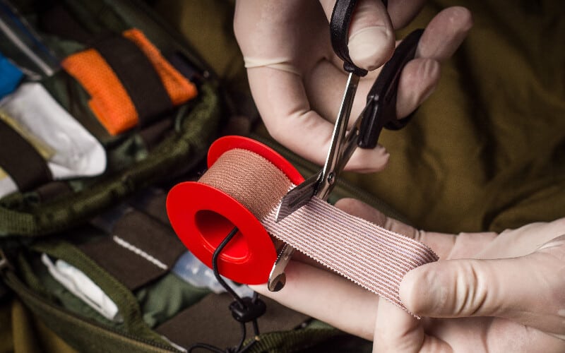 Close up of a person using first aid scissors to cut a medical bandage.
