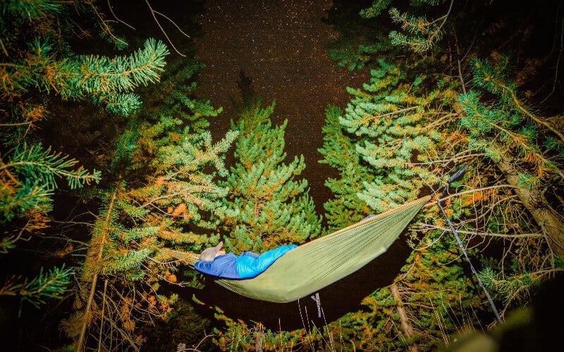 Man asleep in a green hammock under a starry night sky.