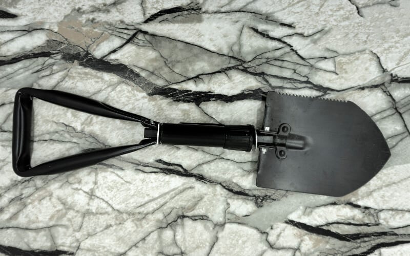 Hiking for beginners essentials: a foldable hiking trowel or shovel on a rock background.